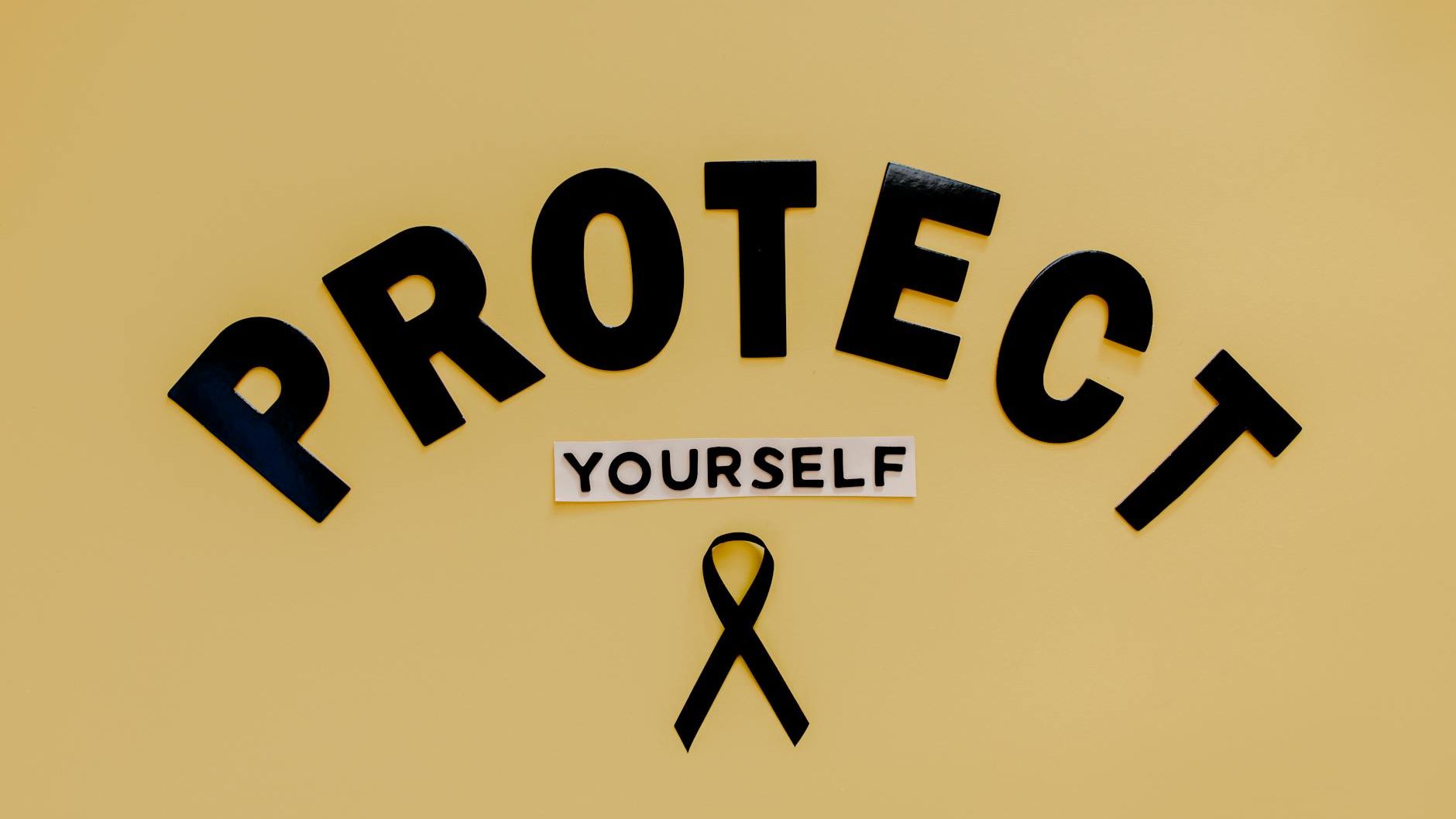 text saying protect yourself and a skin cancer symbol black ribbon lying on brown background